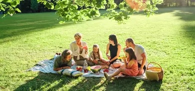 Gruppe von Erwachsenen und Kindern auf Picknickdecke mit Obst und Getränken auf Wiese