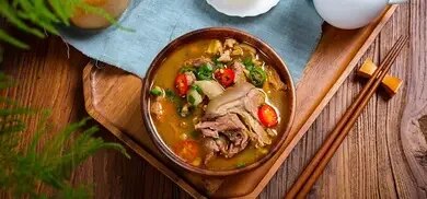 Schale mit Suppe, Fleischstücken, Chili und Frühlingszwiebeln auf Holztablett neben Essstäbchen
