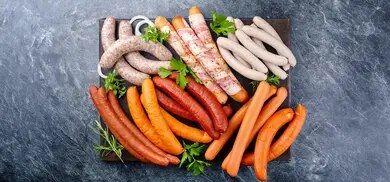 Verschiedene rohe und gegarte Wurstsorten auf Platte mit Kräutern und Zwiebelscheiben
