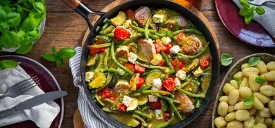 Zucchini-Filet-Pfanne mit grünen Bohnen, Kirschtomaten und Feta in einer Pfanne auf Holztisch