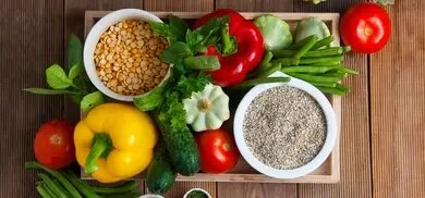 Tablett mit Linsen, Getreide, Paprika, Bohnen, Tomaten, Zucchini und Kräutern auf Holztisch