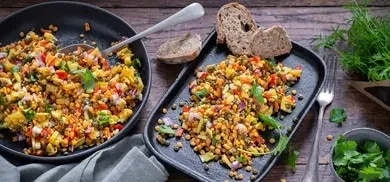 Mango-Linsen-Salat mit Paprika und Zwiebeln in Schale und auf Teller, dazu Brotscheiben und Koriander