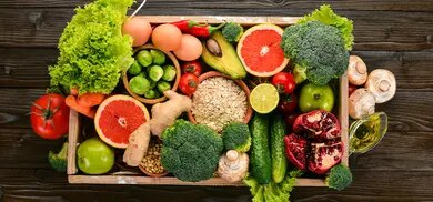 Kiste mit Obst, Gemüse, Haferflocken, Avocado, Brokkoli, Eiern und Olivenöl auf Holztisch