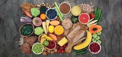 Obst, Gemüse, Vollkornbrot, Haferflocken, Hülsenfrüchte, Nüsse und Samen auf Steinoberfläche