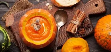 Kürbissuppe in einem ausgehöhlten Kürbis auf einem Holzbrett mit Löfel
