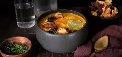 Kürbissuppe mit Gemüsechips, Limettenscheibe und Dill in dunkler Schale