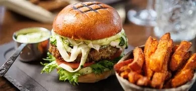 Ein Burger mit Süßkartoffel-Pommes und einem Dip, angerichtet auf einer dunklen Platte