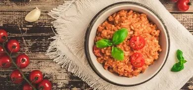 Ein Teller Tomaten-Risotto steht auf einem Holztisch mit Knoblauch und frischen Tomaten daneben