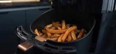 Der herausgezogene Garkorb eines Airfryers, locker gefüllt mit fertigen, goldbraunen Pommes