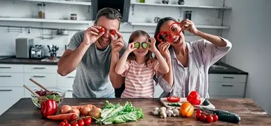 Eine Familie bestehend aus Vater, Mutter und Kind schneiden Gemüse und haben Spaß dabei.