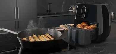 Hähnchengeschnetzeltes, das in einer Pfanne brutzelt, daneben ein Airfryer mit Hähnchenschenkel