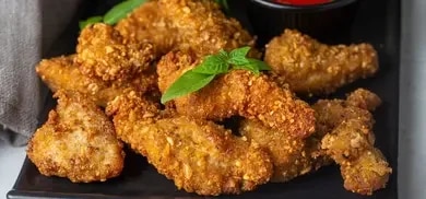Knusprige hausgemachte frittierte Hähnchenstreifen garniert mit Kräutern serviert auf einem Teller mit Dip.