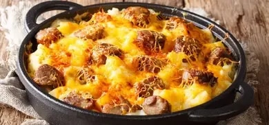 Nudel-Gratin mit Würstchen und überbackenem Käse in einer Pfanne serviert.