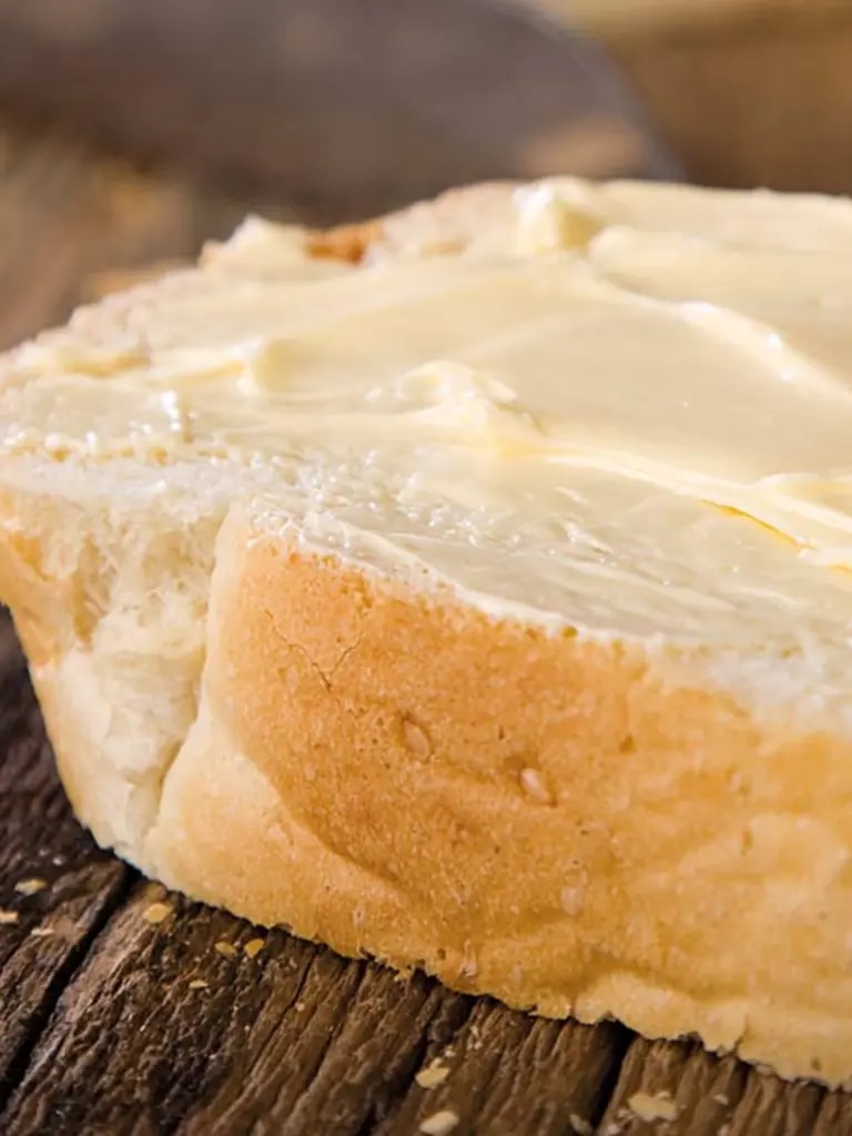 Margarine auf Baguettescheibe geschmiert, die auf einem Holzbrett liegt