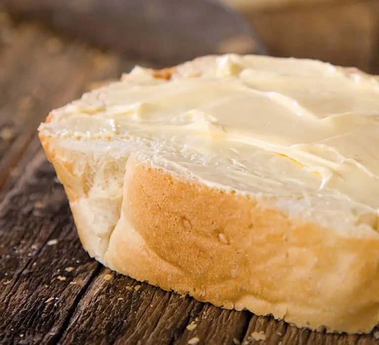 Margarine auf Baguettescheibe geschmiert, die auf einem Holzbrett liegt