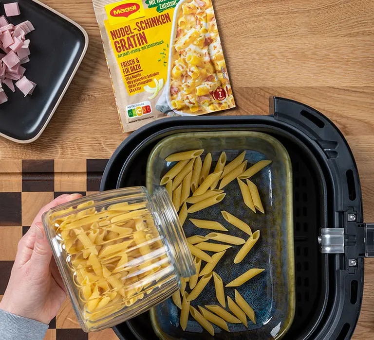 Nudeln die in den Korb einen Airfryers geschüttet werden 