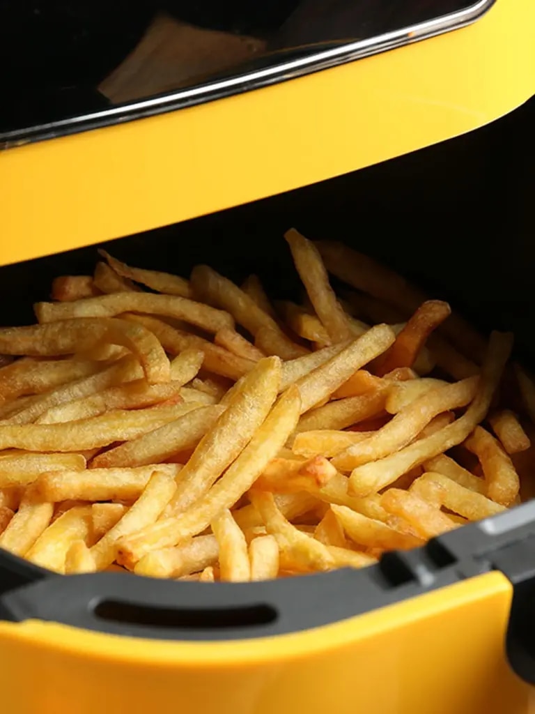 Eine moderne Heißluftfritteuse in einer hellen, freundlichen Küche. Aus dem geöffneten Korb quellen goldbraune Pommes