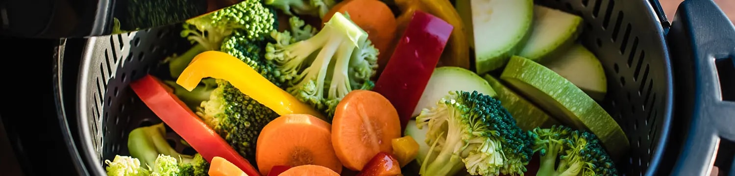 Ein bunter Mix aus verschiedenen Gemüsesorten wie Brokkoli, Karotten, Paprika und Zucchini liegt im Korb einer Heißluftfritte