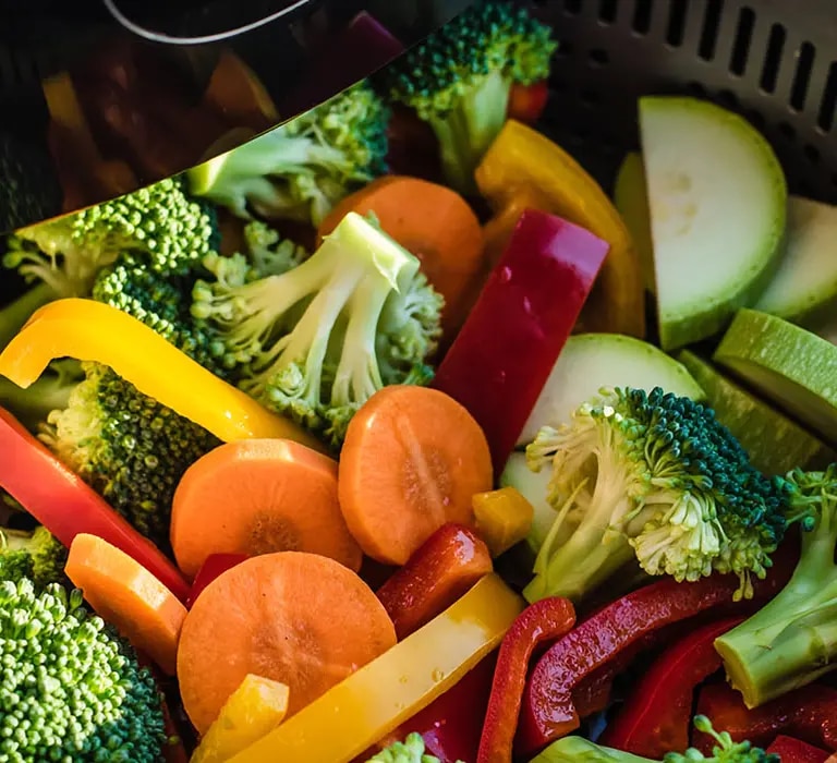 Ein bunter Mix aus verschiedenen Gemüsesorten wie Brokkoli, Karotten, Paprika und Zucchini liegt im Korb einer Heißluftfritte