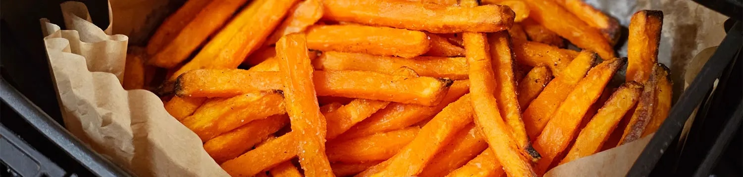 Süßkartoffel-Pommes in einem mit Backpapier ausgelegten Korb eines Airfryers