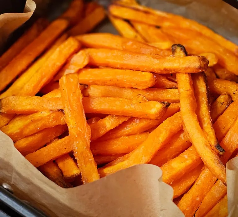 Süßkartoffel-Pommes in einem mit Backpapier ausgelegten Korb eines Airfryers