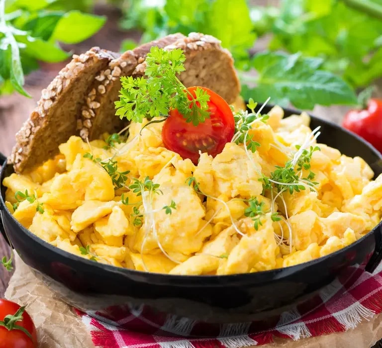 Rührei mit Tomaten und Brot in einer Pfanne, auf einem Tisch serviert