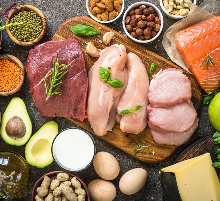 Auf einer dunklen Oberfläche liegen verschiedene proteinreiche Lebensmittel dekorativ angeordnet, darunter roher Lachs, Hähnc