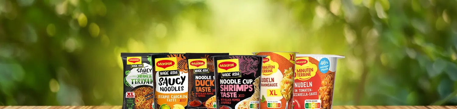 Mehrere Maggi Instantnudeln und Noodle Cups auf Holztisch vor unscharfem grünem Hintergrund