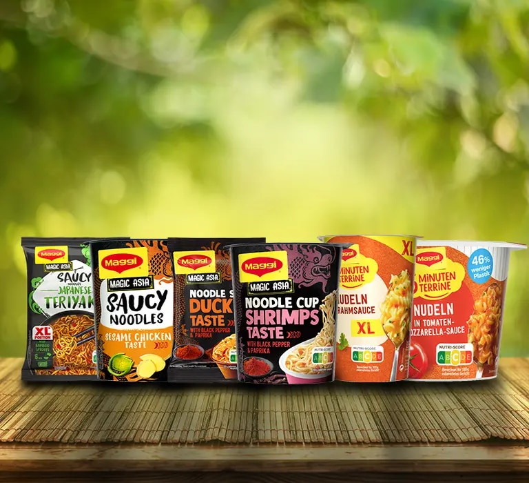 Mehrere Maggi Instantnudeln und Noodle Cups auf Holztisch vor unscharfem grünem Hintergrund