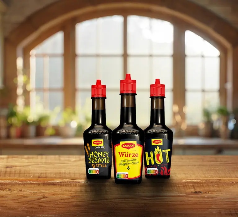 Drei Maggi Saucenflaschen auf Holztisch, Sorten Honey Sesame Style, Würze Das Original und Hot Chili, Küche im Hintergrund