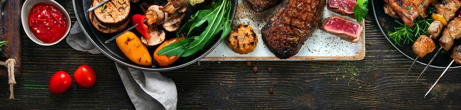 Grillplatte mit Steaks, Gemüsespießen, Saucen und Brot auf dunklem Tisch angerichtet