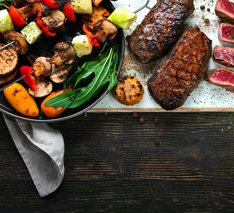 Grillplatte mit Steaks, Gemüsespießen, Saucen und Brot auf dunklem Tisch angerichtet