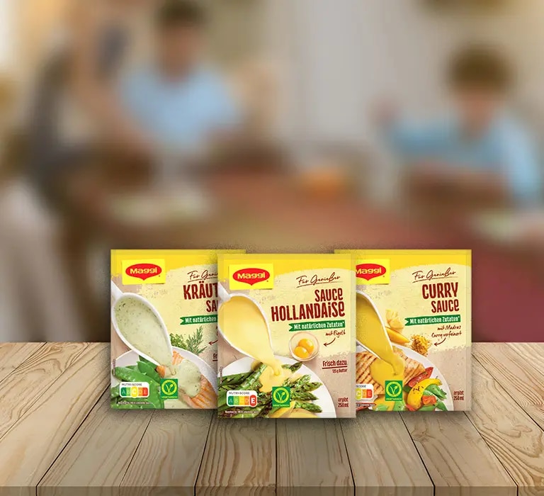 Drei Maggi Saucenpackungen mit Kräutersauce, Sauce Hollandaise und Currysauce auf Holztisch vor Küche