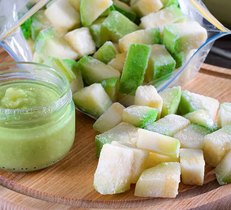 Gefrorene Zucchiniwürfel in Beutel und Schale mit Zucchinipüree im Glas auf Holzbrett