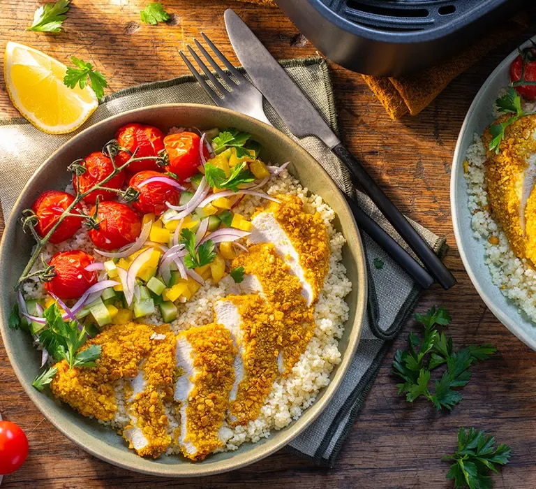 Zwei Schalen mit paniertem Hähnchenschnitzel auf Couscous, Cherrytomaten, roten Zwiebeln und Gurkenwürfeln