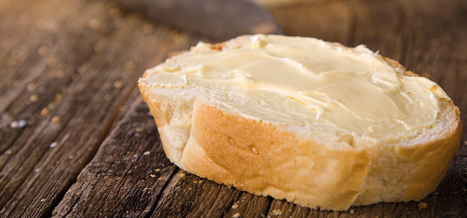 Margarine auf Baguettescheibe geschmiert, die auf einem Holzbrett liegt