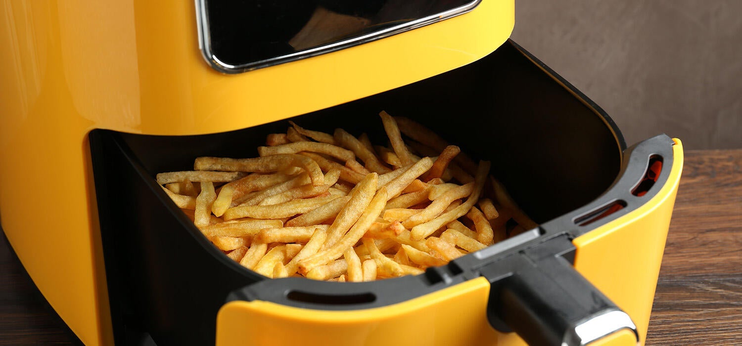 Eine moderne Heißluftfritteuse in einer hellen, freundlichen Küche. Aus dem geöffneten Korb quellen goldbraune Pommes