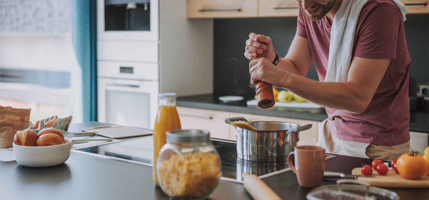 Eine Person steht in einer Küche und würzt eine Speise in einem Topf auf dem Herd.