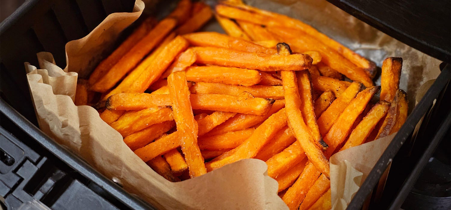 Süßkartoffel-Pommes in einem mit Backpapier ausgelegten Korb eines Airfryers
