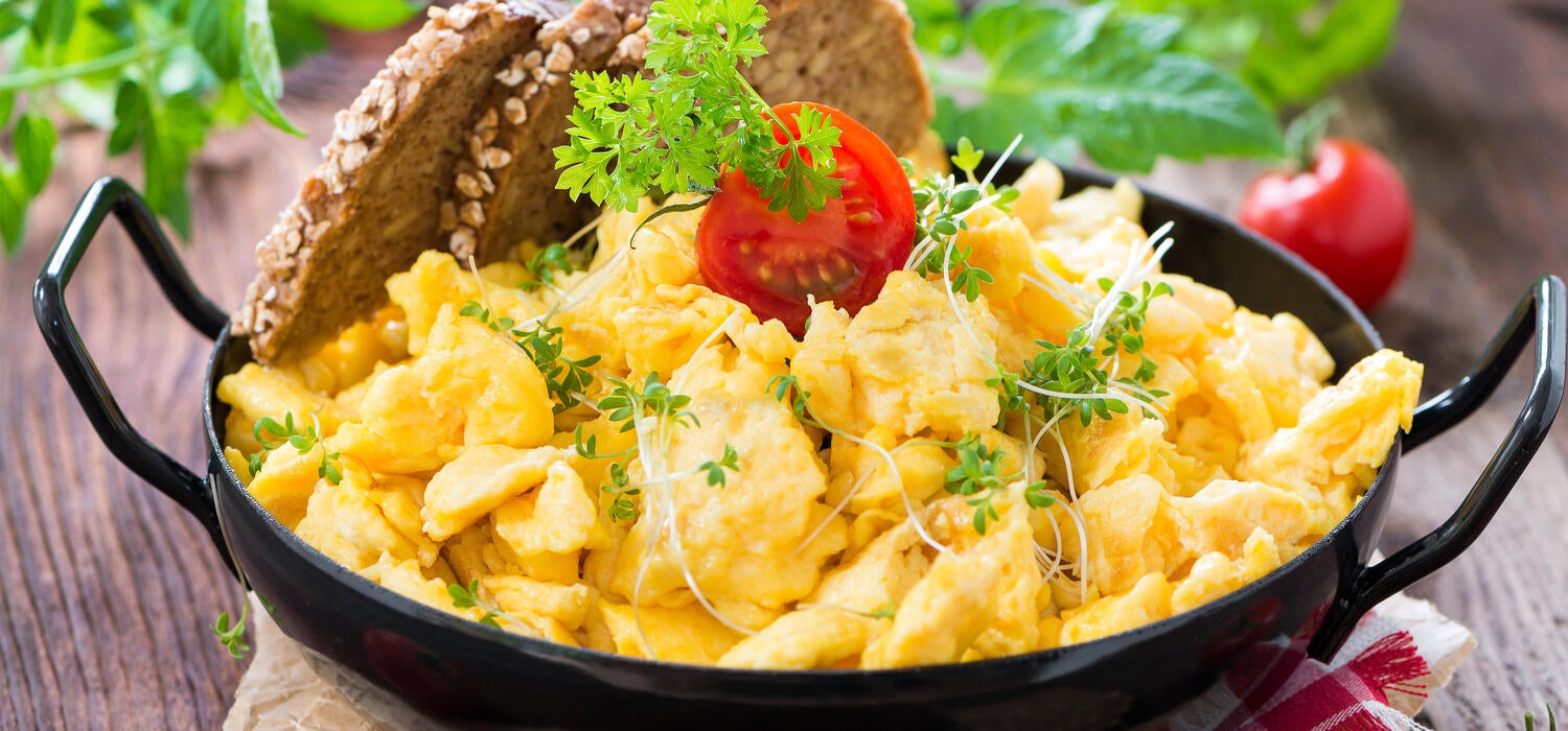 Rührei mit Tomaten und Brot in einer Pfanne, auf einem Tisch serviert