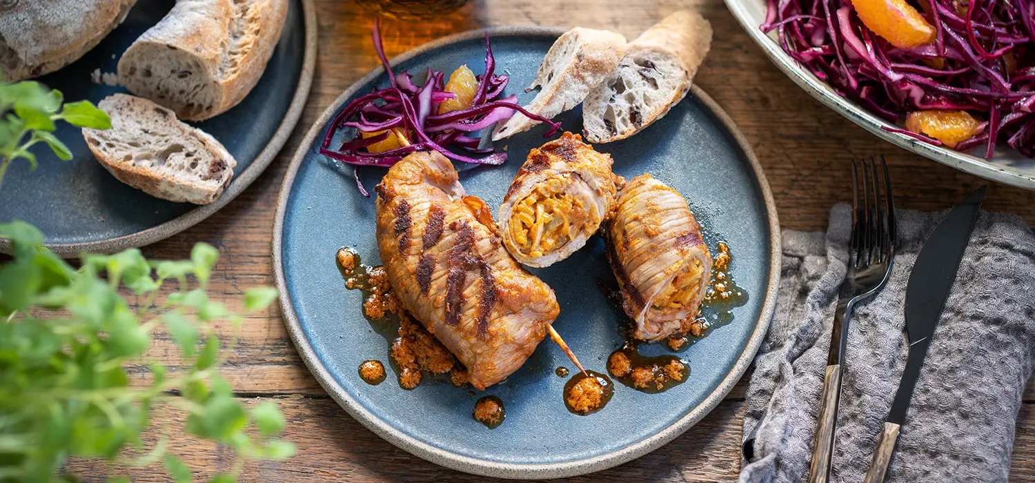 Gegrillte Fleischrouladen auf Teller mit Brotscheiben und Rotkohlsalat auf Holztisch