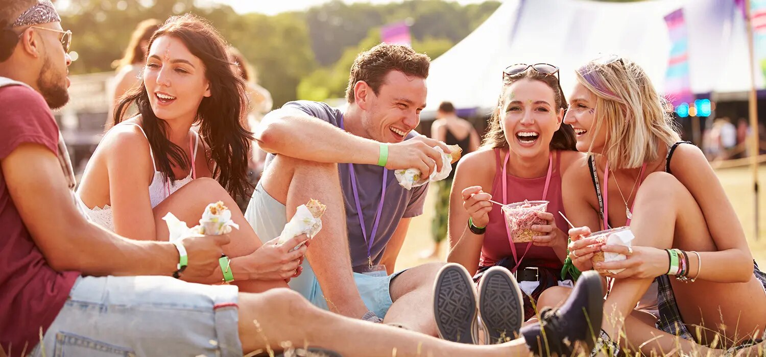 Gruppe sitzt auf Wiese bei Festival und isst Snacks aus Bechern und Wraps