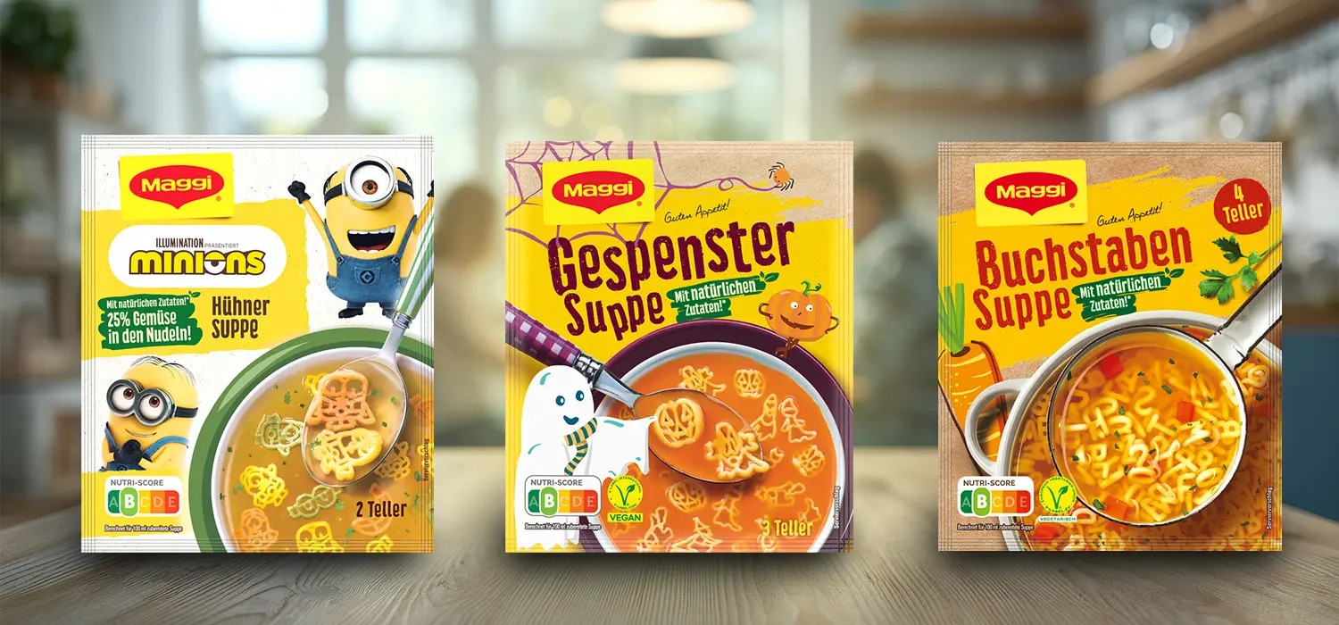 Drei Maggi Suppenpackungen mit Minions Huehnersuppe, Gespenstersuppe und Buchstabensuppe auf Holztisch
