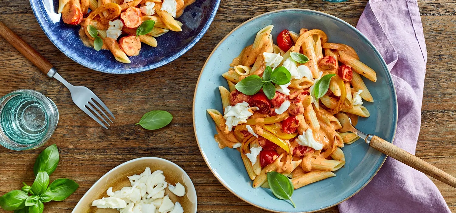 Penne mit Tomatensauce, Basilikum und Kaeseflocken auf Tellern auf Holztisch