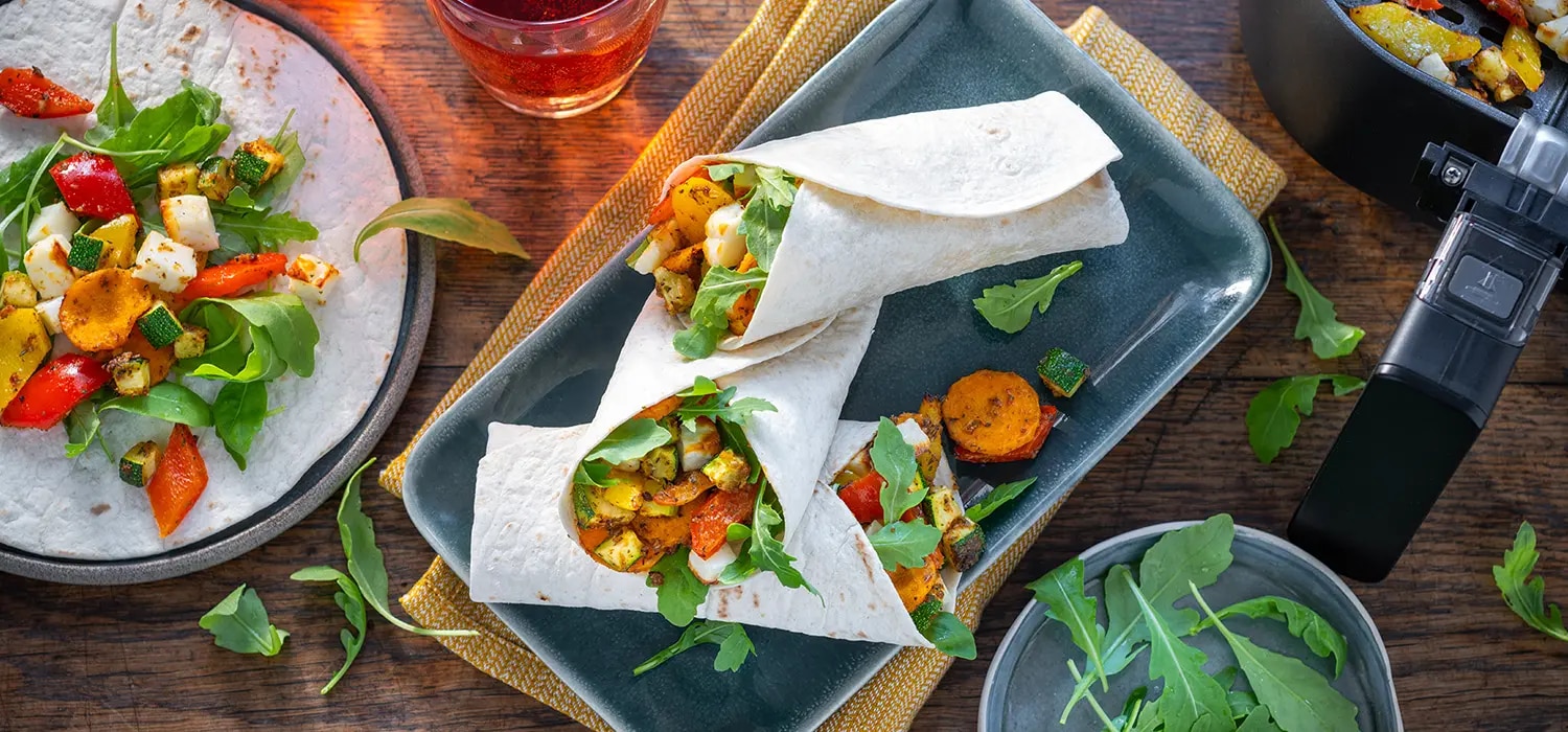 Wraps mit Halloumi, gegrilltem Gemuese und Rucola auf Teller und Platte auf Holztisch