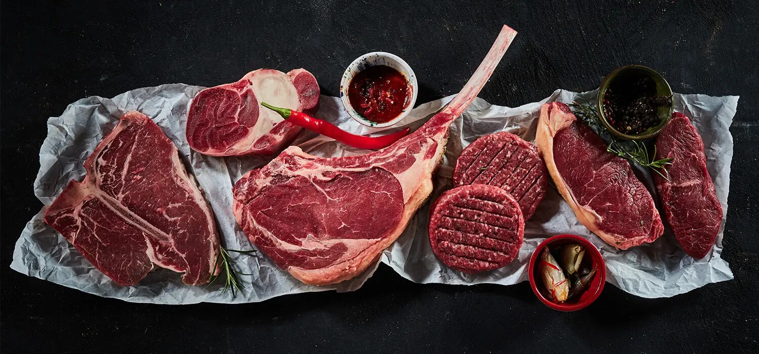 Verschiedene rohe Rindfleischstücke, Steaks und Hackfleisch mit Gewürzen auf dunklem Untergrund angerichtet
