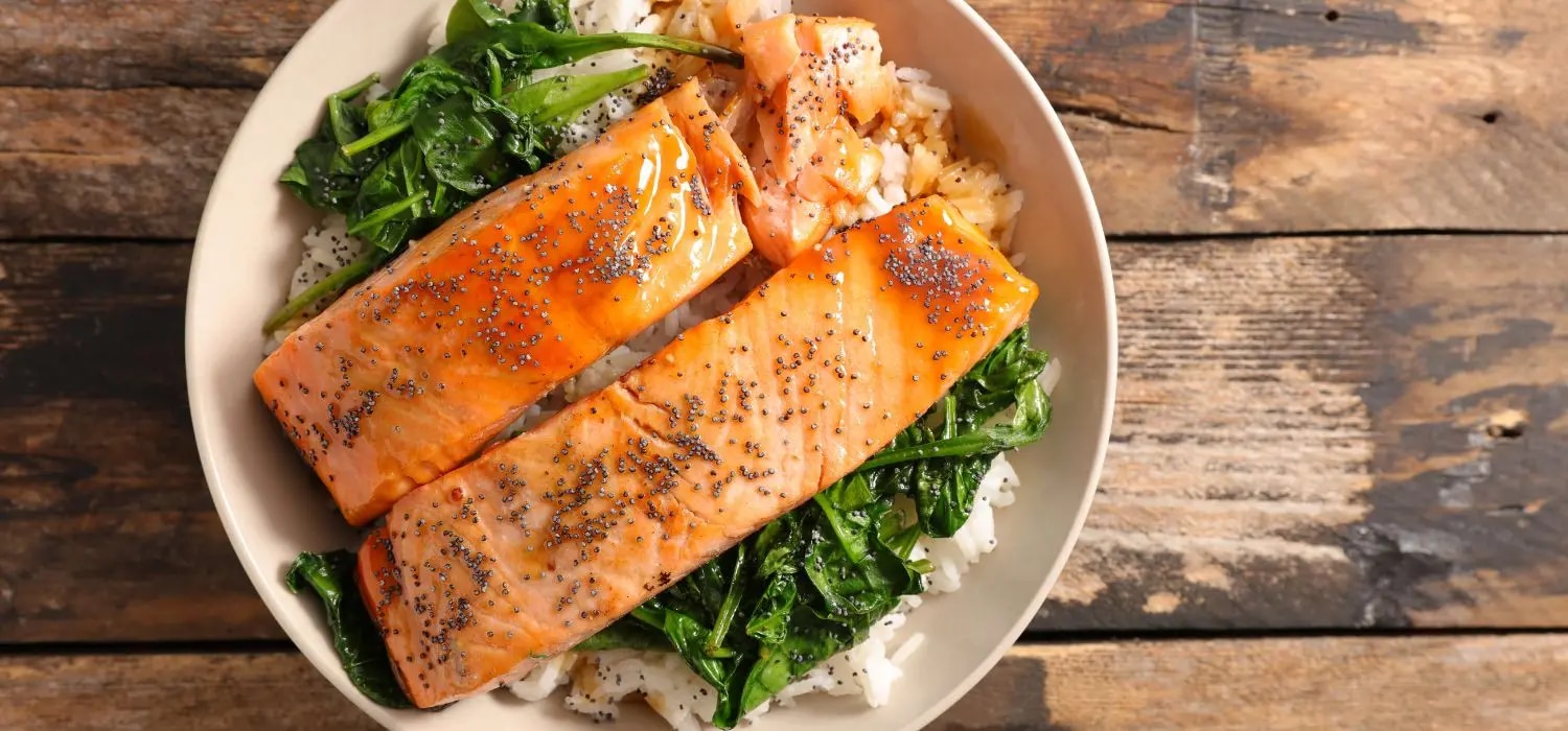 Lachs mit Spinat und Teriyaki-Sauce garniert mit Sesam serviert auf Reis in einer Schüssel.