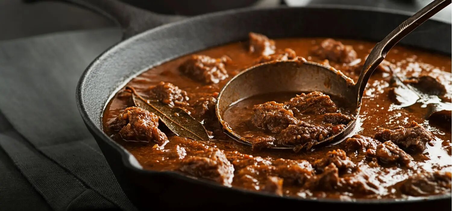 Rindergulasch in einer Pfanne serviert und einer Kelle.