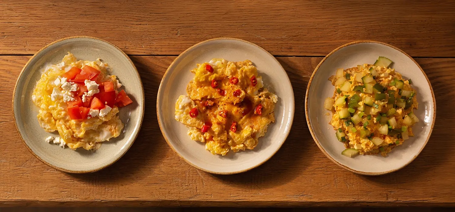 Drei kleine Teller mit verschiedenen Rührei-Variationen: eine mit Tomate/Feta, eine mit Chili/Maggi Würze Hot und eine mit Gemüse