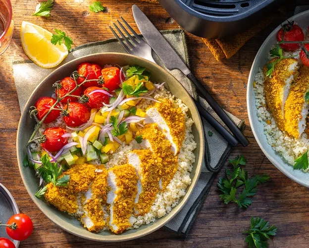 Zwei Schalen mit paniertem Hähnchenschnitzel auf Couscous, Cherrytomaten, roten Zwiebeln und Gurkenwürfeln